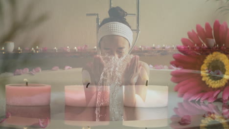 Animation-of-pink-flower-and-candles-over-happy-biracial-woman-splashing-face-in-bathtub