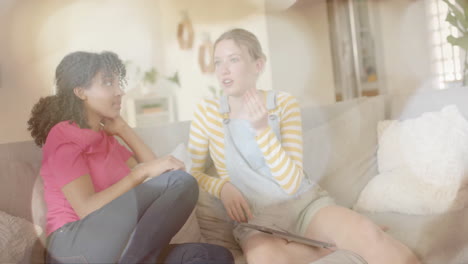 Animation-Von-Lichtpunkten-über-Zwei-Unterschiedlichen-Teenager-Mädchen,-Die-Auf-Der-Couch-Reden