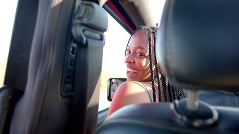 Young-African-American-woman-smiles-from-the-driver's-seat-on-a-road-trip,-with-copy-space