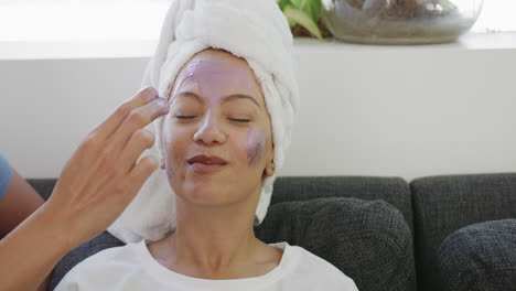Young-biracial-woman-applies-facial-mask-at-home,-with-copy-space