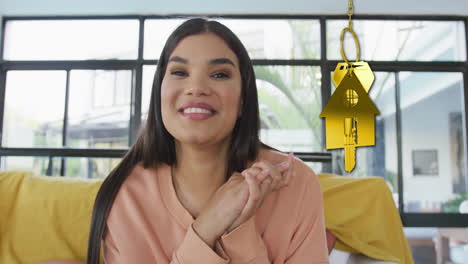 Animation-of-gold-house-key-and-key-fob-over-happy-biracial-woman-at-home