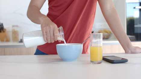 Person-pours-milk-into-a-bowl-of-cereal-at-a-kitchen-counter