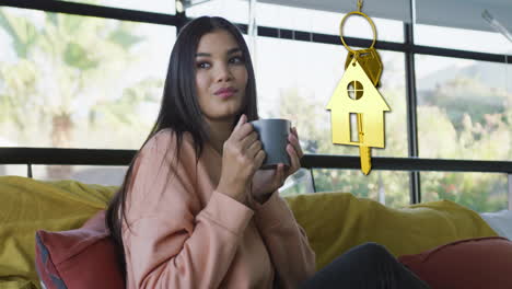 Animation-of-gold-house-key-and-key-fob-over-diverse-woman-dinking-tea-at-home