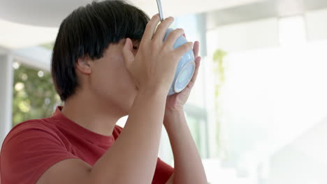 Teenage-Asian-boy-drinks-from-a-cup-in-a-bright-kitchen-at-home-with-copy-space