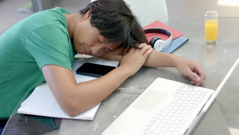 Teenage-Asian-boy-rests-his-head-on-a-desk-while-studying,-with-copy-space