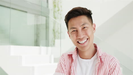 A-young-Asian-man-smiles-brightly-at-home-in-a-modern-indoor-setting-with-copy-space