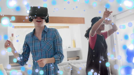 Animation-of-blue-and-white-spots-over-two-happy-diverse-teenage-girls-in-dancing-in-vr-headsets