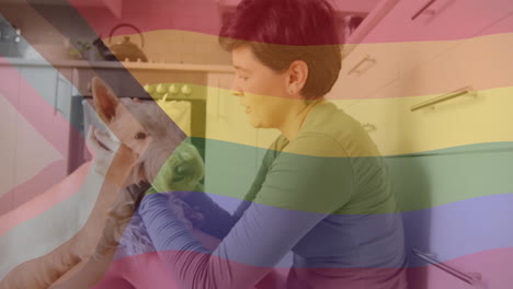 Animation-of-pride-rainbow-flag-over-happy-caucasian-petting-pet-dog-in-kitchen