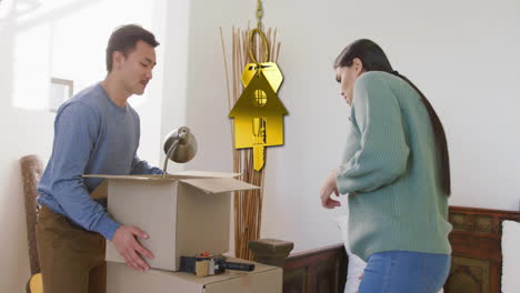 Animation-of-golden-key-and-house-over-diverse-couple-carrying-cartons-at-home