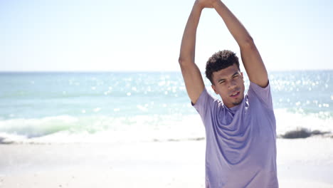 Young-biracial-man-stretches-his-arms-on-a-sunny-beach
