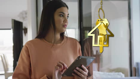 Animation-of-gold-house-key-and-key-fob-over-happy-biracial-woman-using-tablet-at-home
