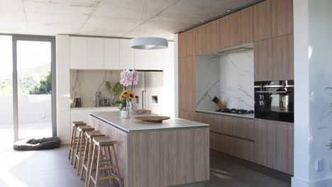 A-modern-kitchen-features-wood-grain-cabinetry-and-a-central-island-with-bar-stools