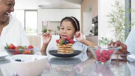 A-biracial-child-admires-a-stack-of-pancakes-topped-with-berries-at-a-kitchen-table