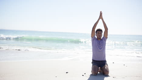 A-young-biracial-man-practices-yoga-on-a-sunny-beach-with-copy-space