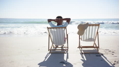 A-young-biracial-man-relaxes-on-a-beach-chair,-facing-the-ocean,-suggesting-a-moment-of-tranquility-