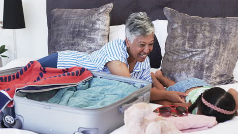 Biracial-woman-with-short-gray-hair-laughs-while-packing-a-suitcase