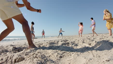 Diverse-friends-playing-a-game-of-soccer-on-a-sandy-beach,-with-copy-space