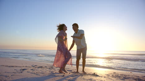 Biracial-couple-enjoys-a-playful-walk-on-the-beach-at-sunset