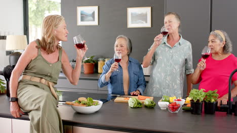 Senior-diverse-group-of-women-enjoy-wine-and-salad-in-a-modern-kitchen