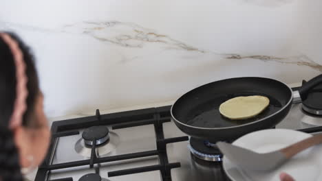 A-biracial-woman-is-cooking-pancakes-on-a-stove,-with-a-focus-on-the-frying-pan