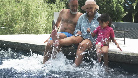 Großeltern-Mit-Gemischter-Abstammung-Und-Enkelin-Genießen-Das-Planschen-Im-Wasser-Am-Pool