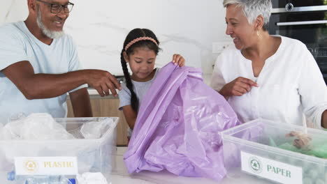 Biracial-family-sorts-recycling,-with-a-granddaughter-placing-plastic-in-a-bin