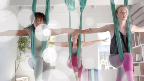 Animation-of-light-spots-over-two-diverse-teenage-girls-doing-aerial-yoga-and-relaxing-at-home