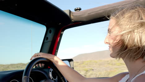 Young-Caucasian-woman-enjoys-a-drive-in-a-convertible-on-a-road-trip,-with-copy-space