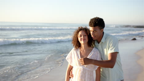 Biracial-couple-enjoys-a-beach-stroll-at-sunset-with-copy-space