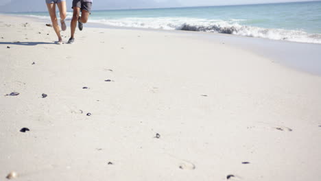 Two-people-are-jogging-along-a-sandy-beach,-leaving-footprints-in-their-wake,-with-copy-space