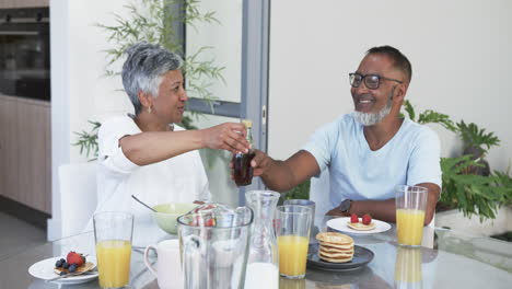 Biracial-couple-enjoys-a-hearty-breakfast,-the-man-opening-a-bottle-of-champagne