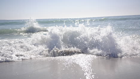 Foamy-waves-crash-onto-the-sandy-shore-under-a-clear-sky-with-copy-space