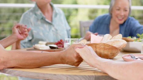 Senior-biracial-woman-holding-hands-with-a-Caucasian-woman-at-a-meal,-with-copy-space