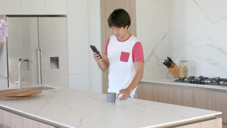 Asiatischer-Teenager-Checkt-Sein-Telefon-In-Einer-Modernen-Küche