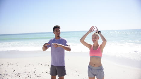 Young-biracial-man-and-Caucasian-woman-stretch-their-arms-up-on-a-sunny-beach