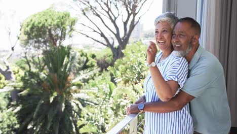 Biracial-couple-enjoys-a-sunny-balcony-view,-with-the-woman-pointing-at-a-distance