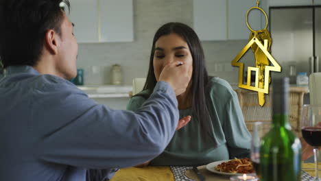 Animation-of-gold-house-key-and-key-fob-over-happy-diverse-couple-eating-at-home