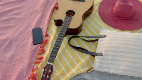 A-guitar-lies-next-to-a-hat-and-phone-on-a-beach-blanket