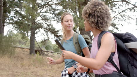 Two-women-are-hiking-in-a-wooded-area,-one-holding-a-smartphone
