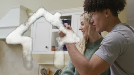 Animation-of-cloud-house-over-happy-diverse-husband-surprising-wife-with-gift-in-kitchen