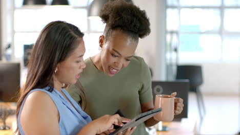 Young-African-American-woman-shares-a-tablet-screen-with-a-biracial-woman-in-a-business-office