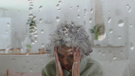 Animation-of-water-droplets-over-senior-african-american-woman-sitting-at-home-with-head-in-hands