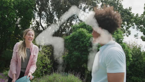 Animation-of-cloud-house-over-happy-diverse-couple-having-pillow-fight-in-garden