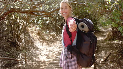 Young-Caucasian-woman-with-a-backpack-smiles-while-hiking-on-a-woodland-trail