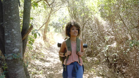 Young-biracial-woman-hikes-on-a-sunny-trail,-sporting-a-backpack
