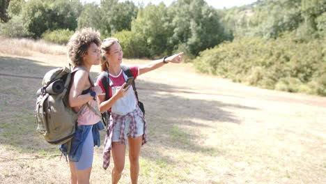 Two-young-women-are-hiking,-one-pointing-out-a-direction-with-copy-space