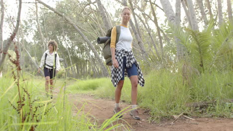 Young-Caucasian-woman-leads-the-way-on-a-forest-hike,-with-a-young-biracial-woman-following
