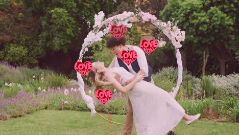 Animation-of-red-love-you-hearts-over-happy-diverse-couple-embracing-in-garden-on-wedding-day