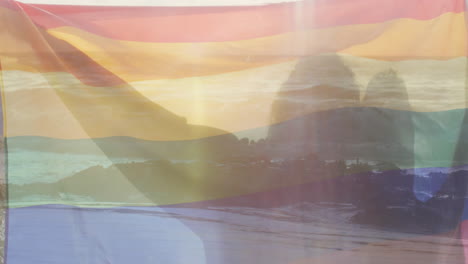 Animation-of-sunset-coast-over-happy-diverse-gay-male-couple-holding-rainbow-flag