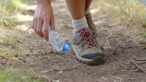 A-person-picks-up-a-plastic-bottle-while-walking-on-a-dirt-path-and-collecting-trash